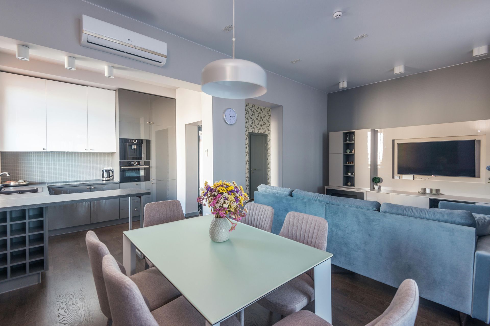 Modern open-plan living room and kitchen with blue sofa, dining table, and wall-mounted TV