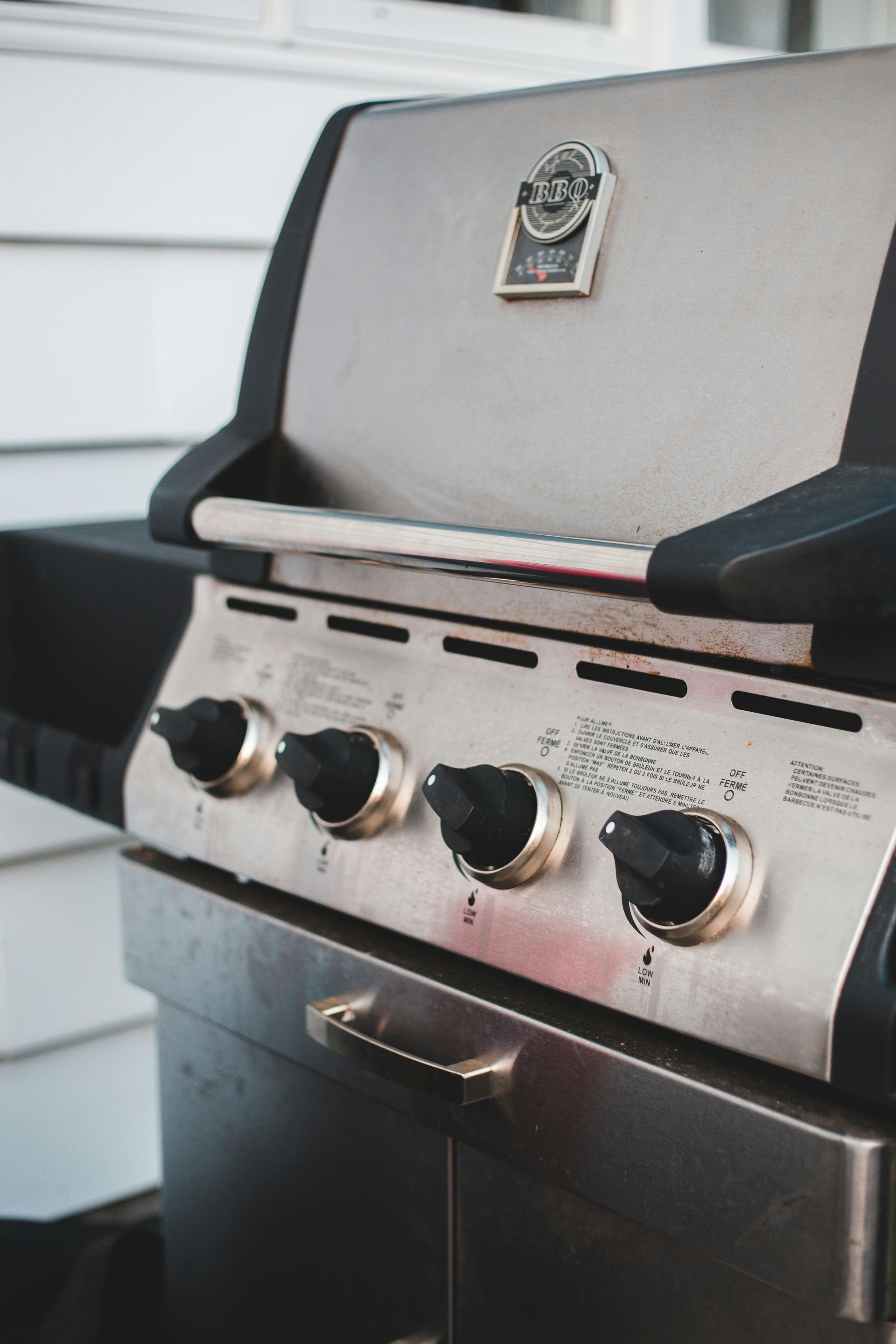 Stainless steel gas grill with three knobs and a closed lid on a patio