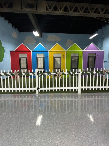 Five colorful playhouses behind a white picket fence on a gray floor.