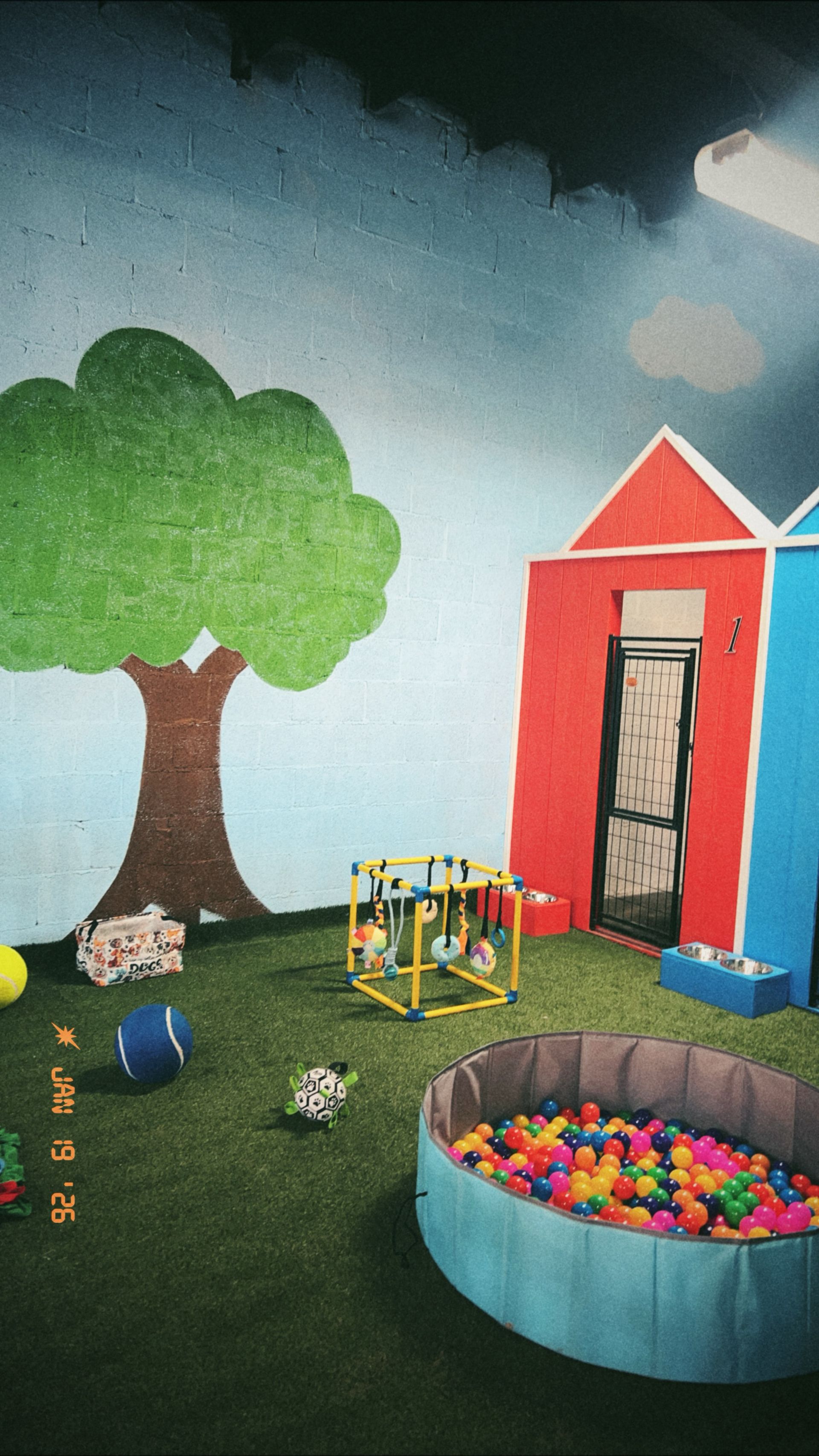Playroom with tree, houses, ball pit, and toy robot under a cloudy sky.