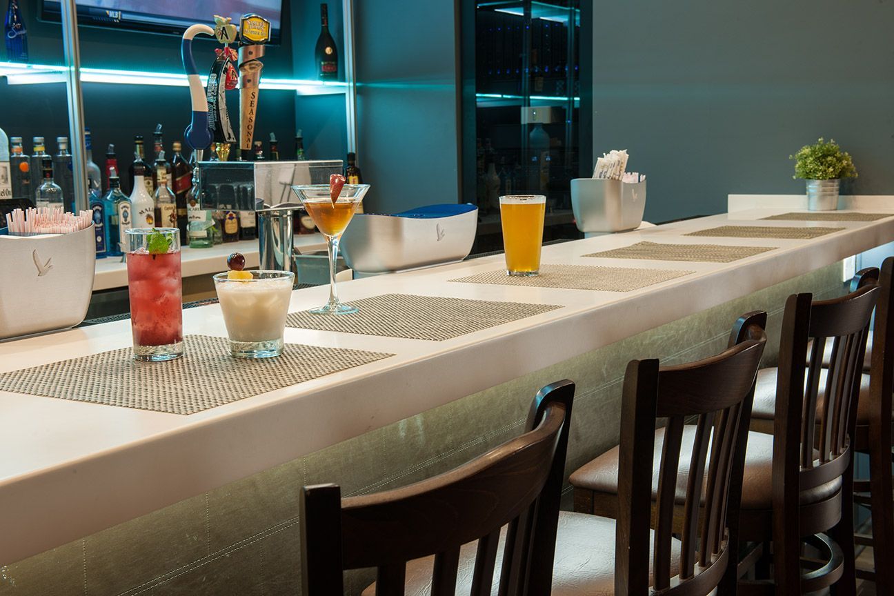 Modern bar counter with colorful cocktails, tall stools, and city lights in the background