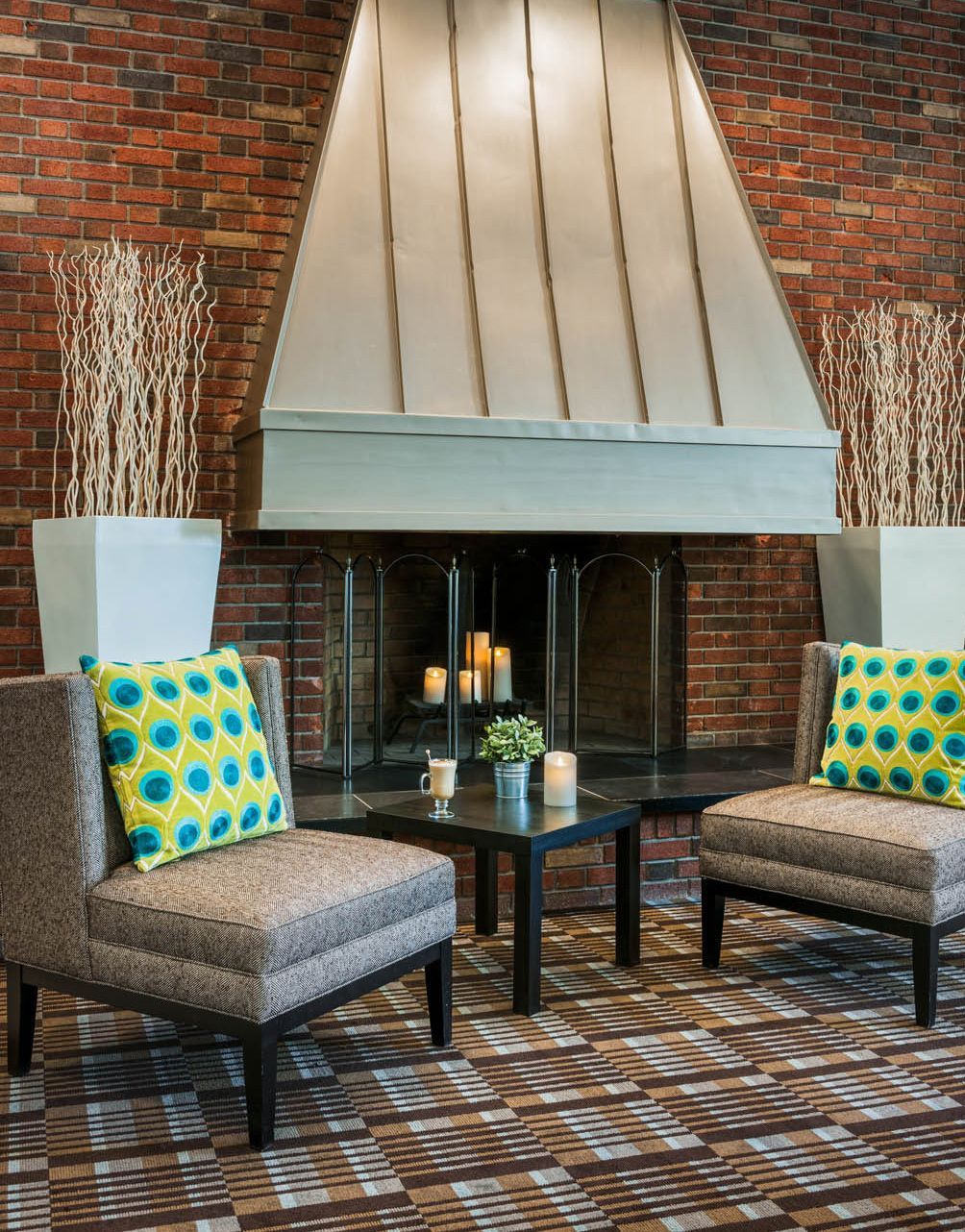 Lounge seating area with brick fireplace, modern chairs, and colorful yellow-blue pillows on a patterned rug.