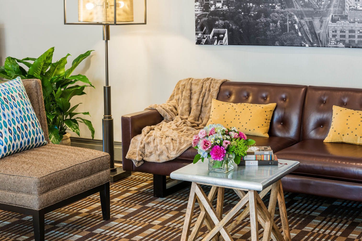Cozy living room with brown leather sofa, patterned chair, floor lamp, coffee table, and flowers