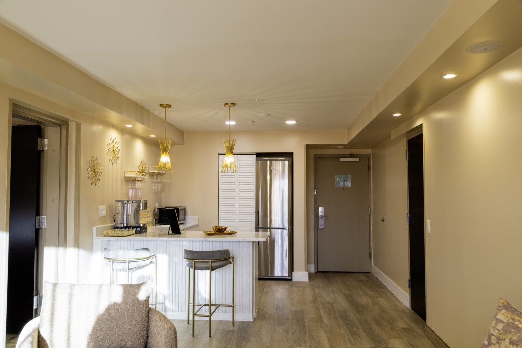 Bright apartment kitchen and living area with white cabinets, bar stools, pendant lights, and wood flooring