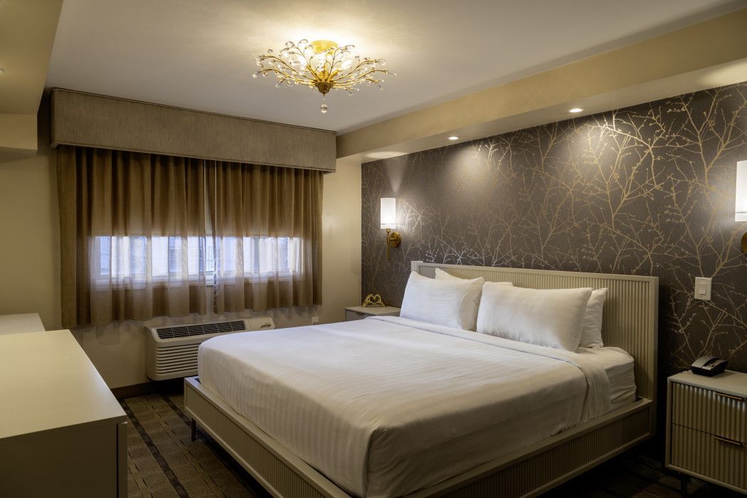 Modern hotel bedroom with a large bed, patterned accent wall, window drapes, and warm lighting