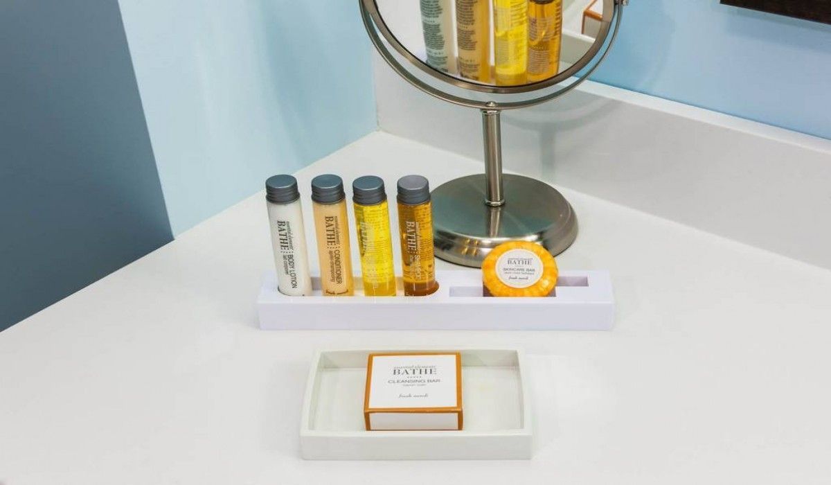 Small vanity display with skincare bottles and a candle on a white tabletop beside a gold lamp.