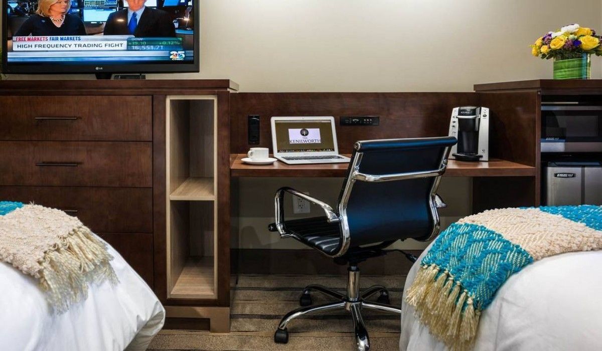 Hotel room workspace with two beds, desk, office chair, TV, and flowers