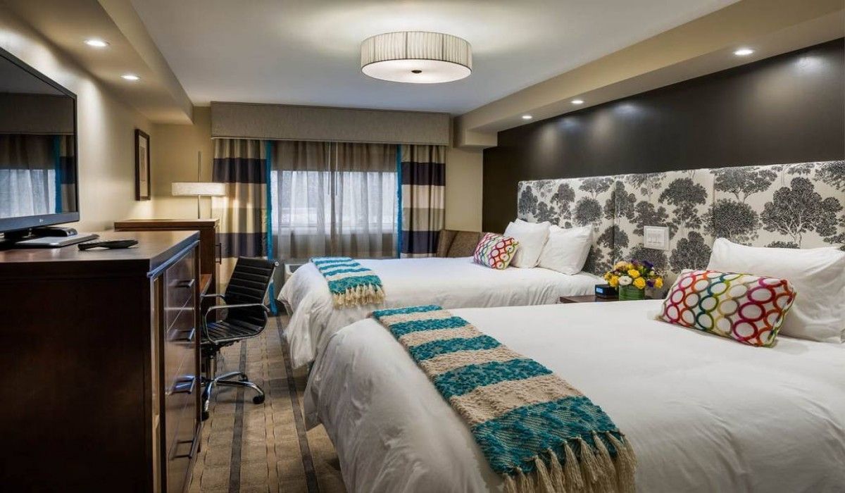 Modern hotel room with two queen beds, turquoise accents, a desk, and a floral accent wall