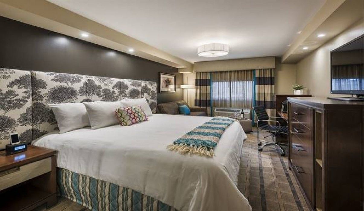 Modern hotel room with a king bed, desk, TV, and large windows with city views