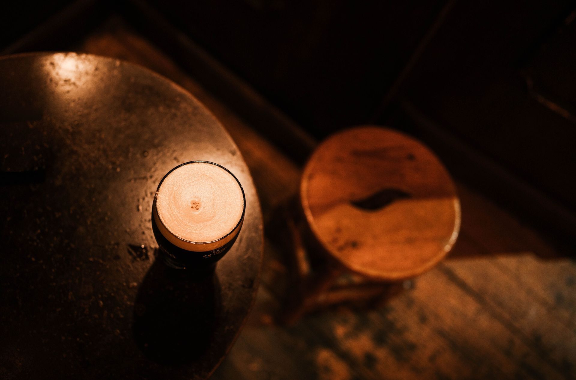 Dimly lit lounge bar with wooden stools, red seating, warm wall lamps, and polished floor