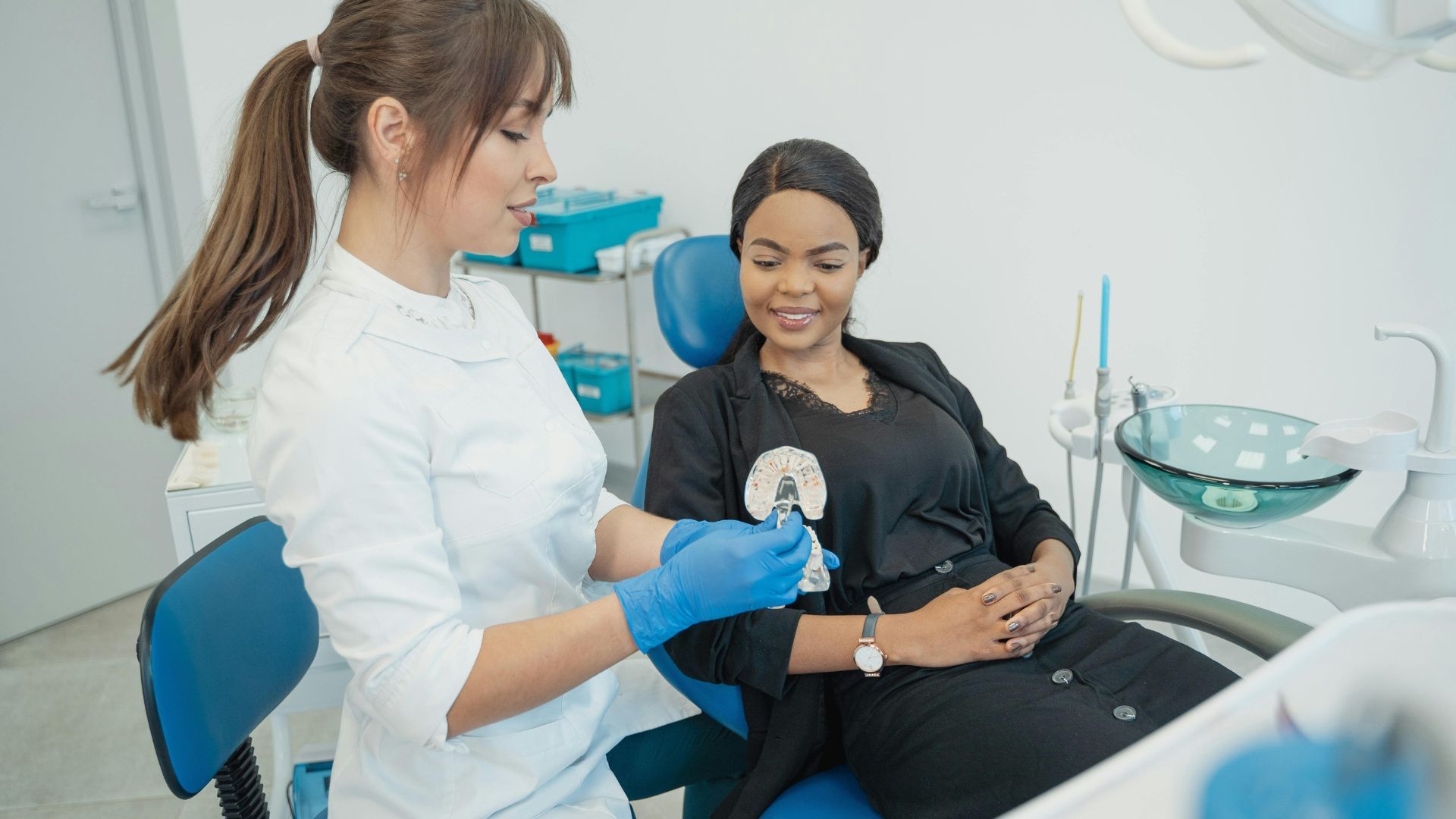 A woman is sitting in a dental chair while a dentist examines her teeth.