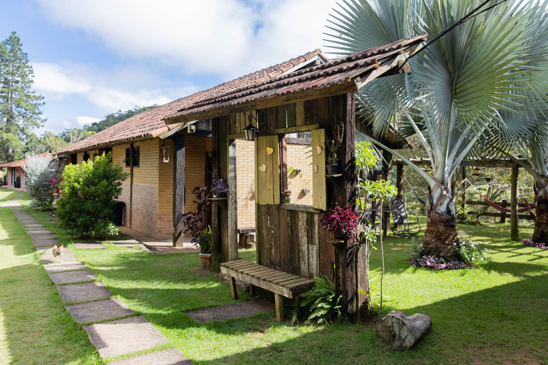Chalé rústico com telhado de telha, varanda sombreada e caminho exuberante em um jardim tropical.