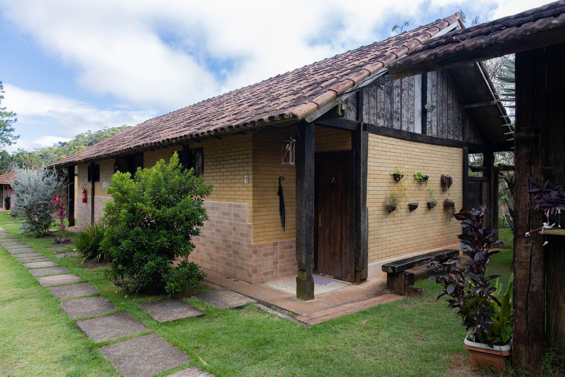Casa rústica de tijolos com telhado de telhas, porta de madeira e gramado verde em um jardim.