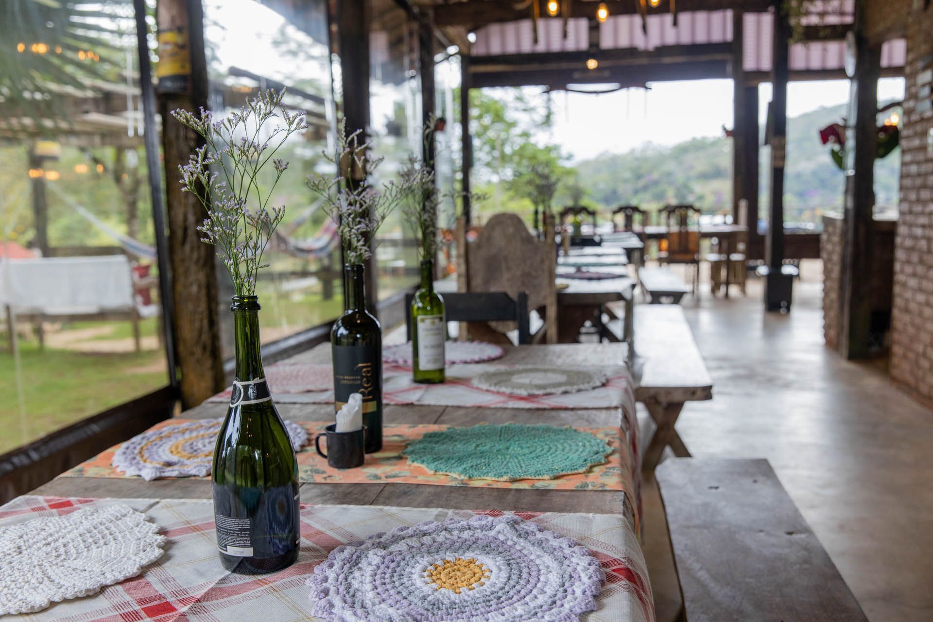 Garrafas de vinho sobre uma mesa estampada em uma área de jantar ao ar livre com vista para uma paisagem verdejante.
