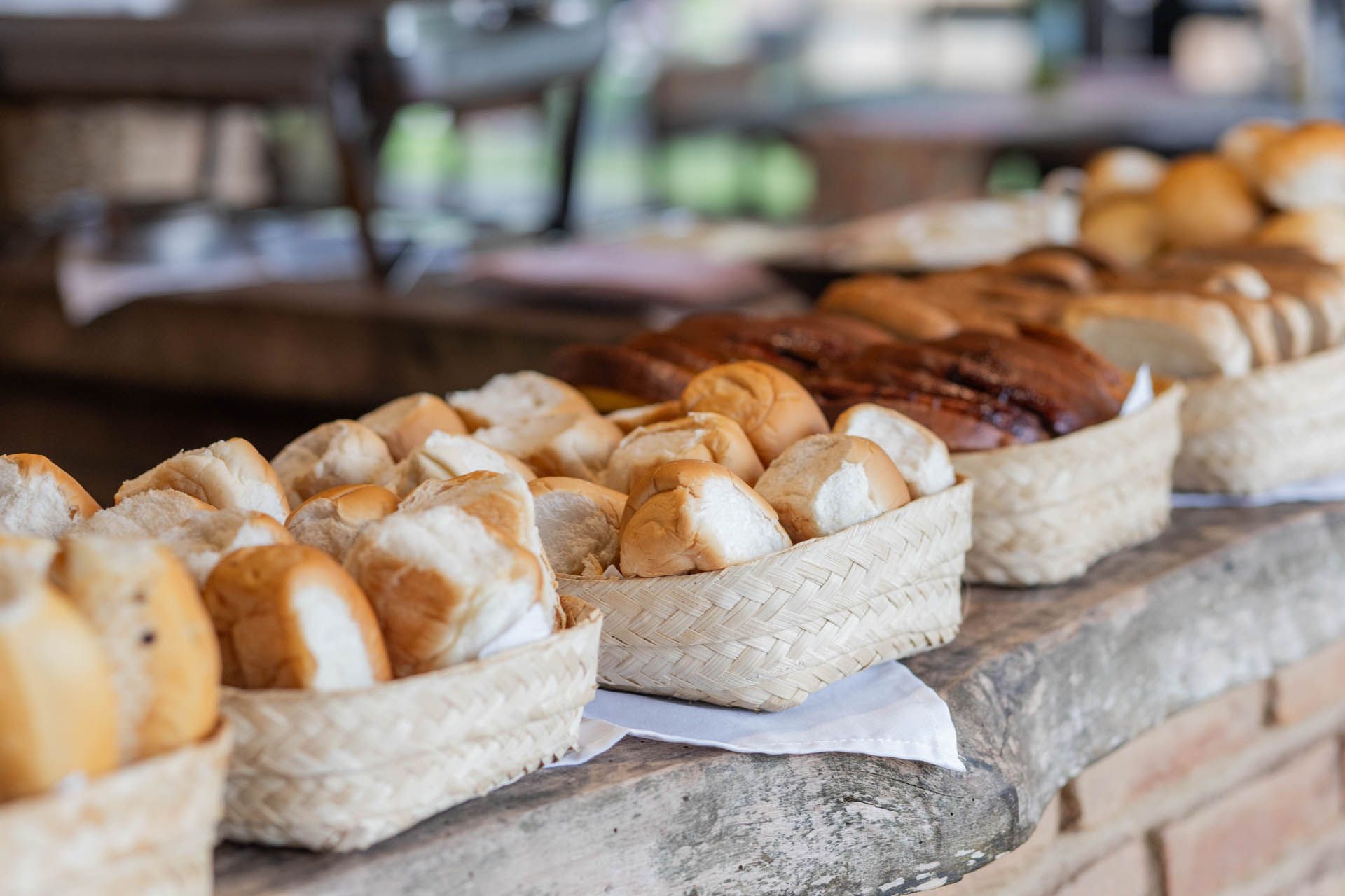 Cestas com diversos tipos de pães e pãezinhos expostas em um balcão de pedra em uma padaria.