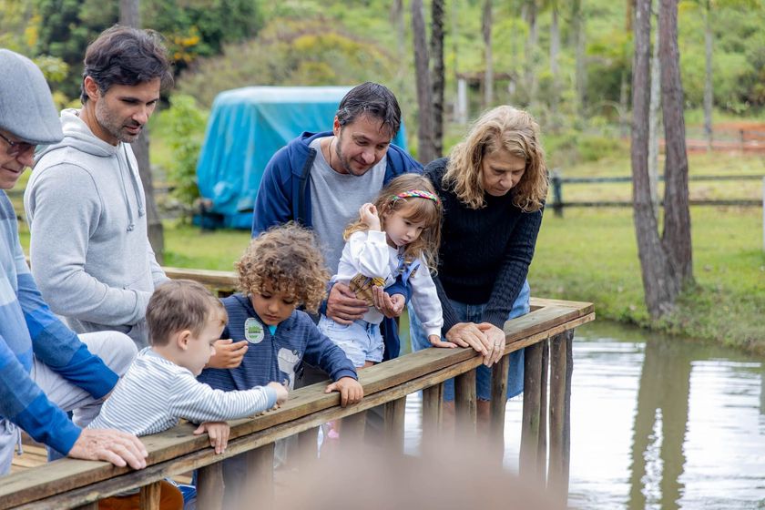 Várias pessoas se debruçam sobre uma grade de madeira, observando a água em um parque.