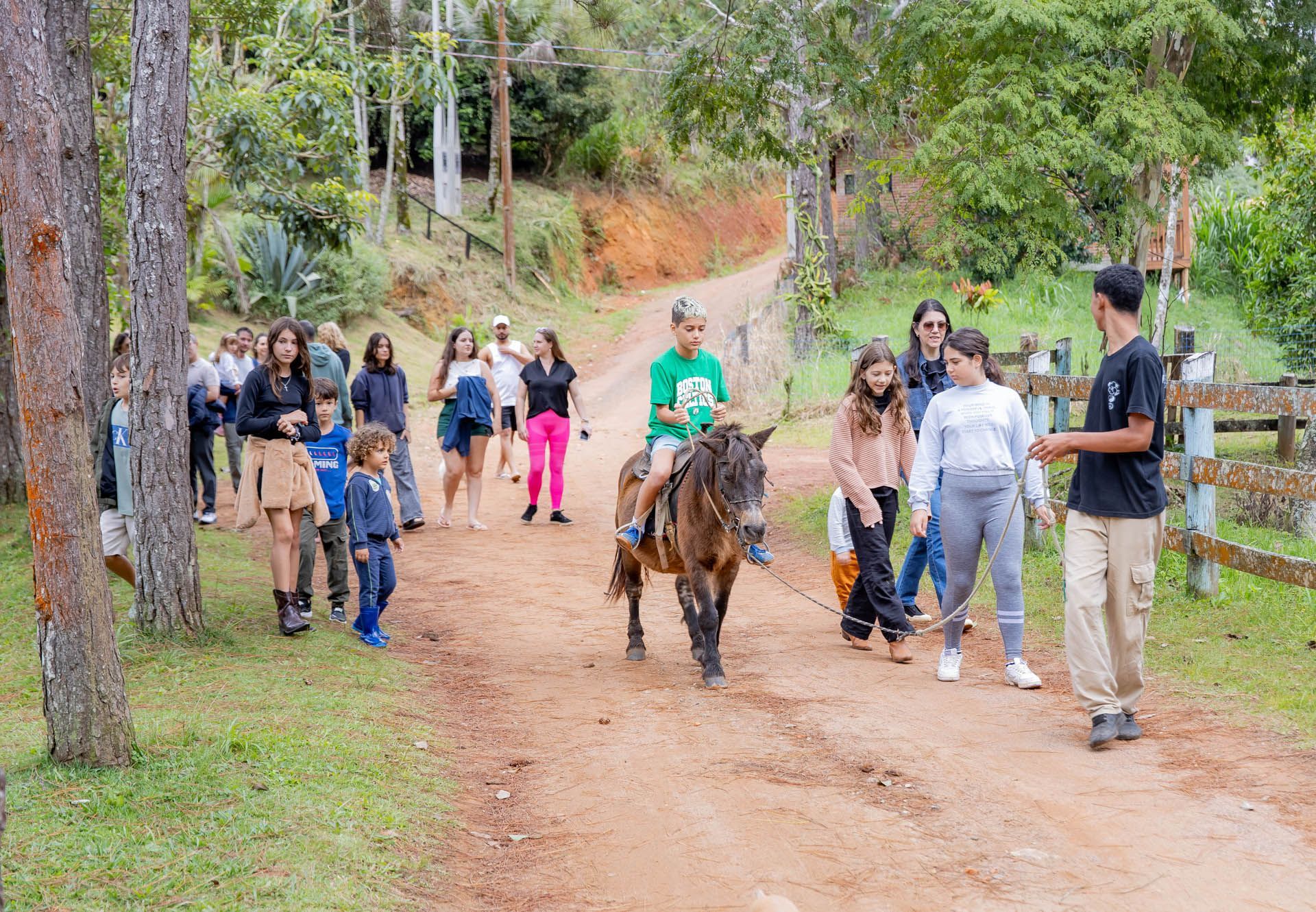 Grupo caminhando com um burro em uma trilha de terra em uma área arborizada do parque.