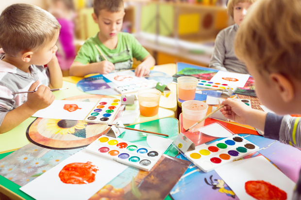 Children painting colorful artwork at a table in a bright classroom