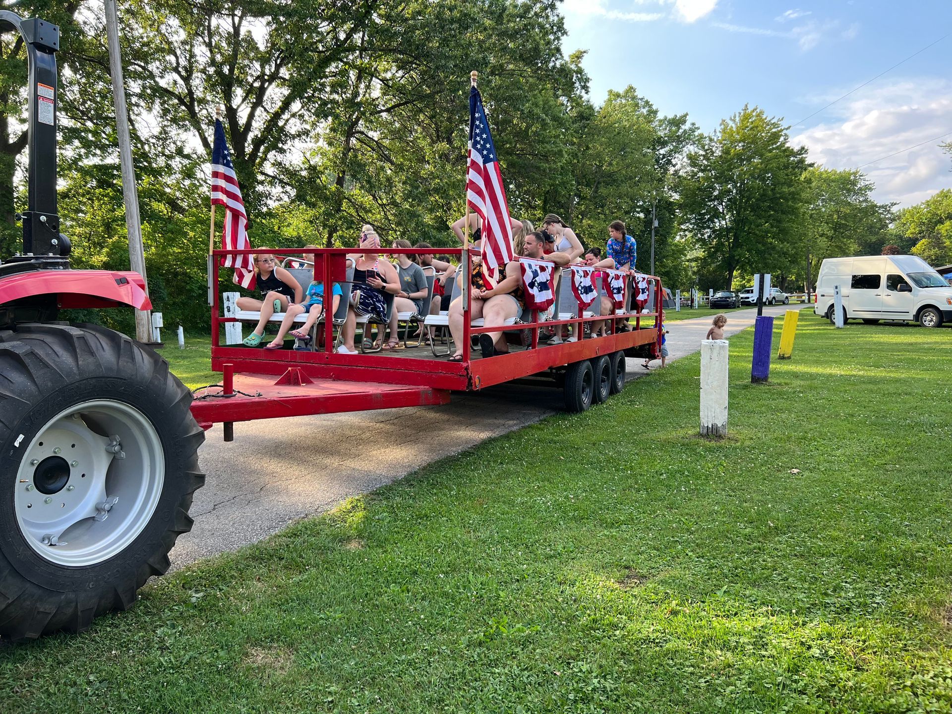 A tractor is pulling a red trailer with people on it.