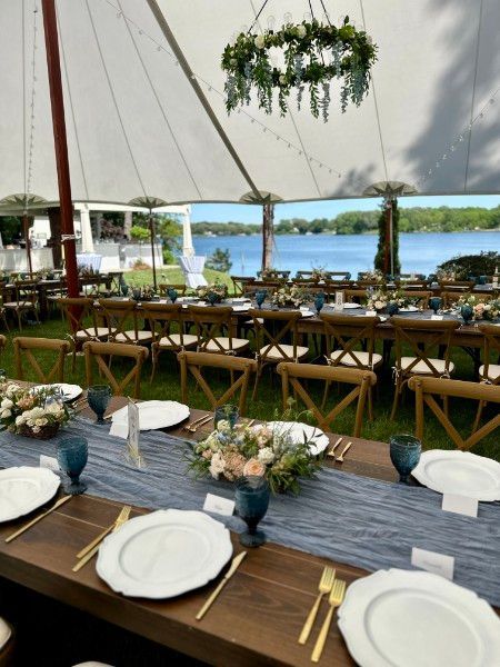 A long table with plates and utensils under a tent with a lake in the background