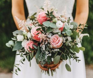 A bride in a white dress is holding a bouquet of pink roses and white flowers.