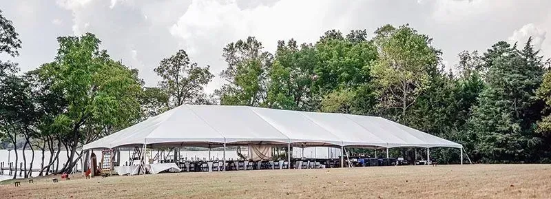 A large white tent set up on a grassy field, with trees in the background, near a body of water.