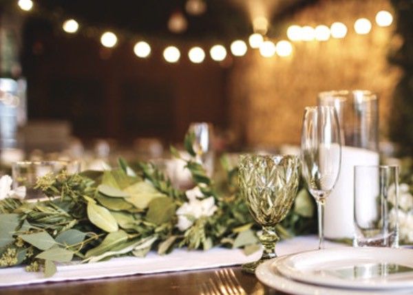 A rented table with plates , glasses , candles and a garland on it.