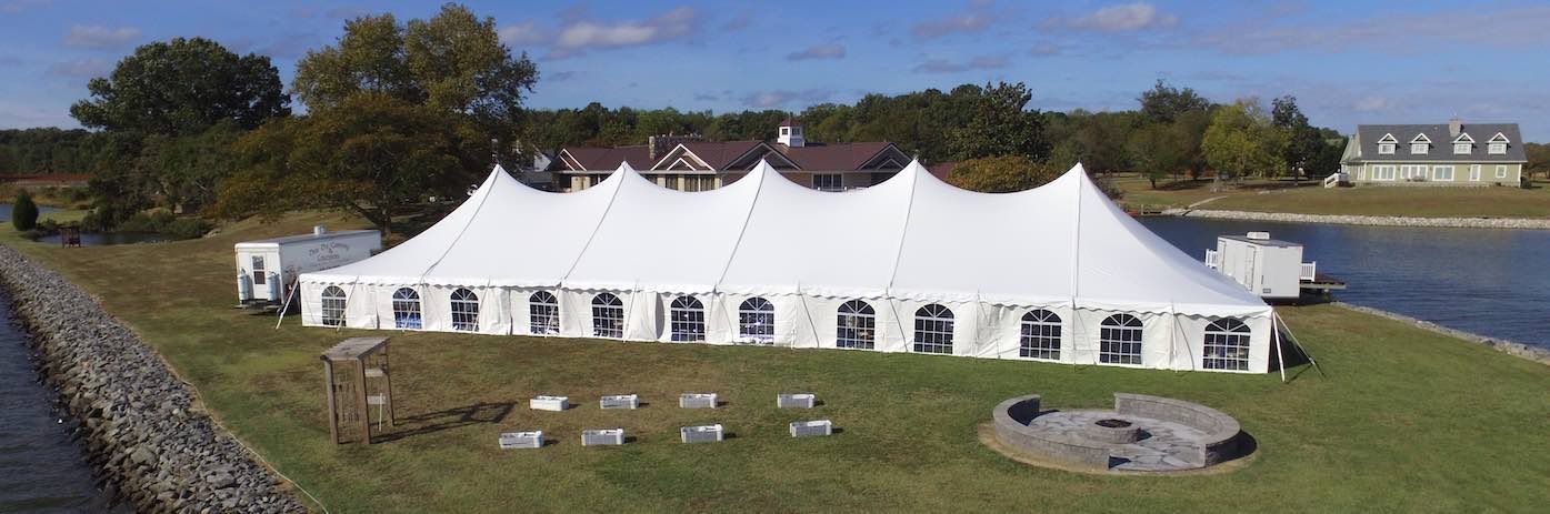 A large white tent is sitting on top of a lush green field next to a body of water.