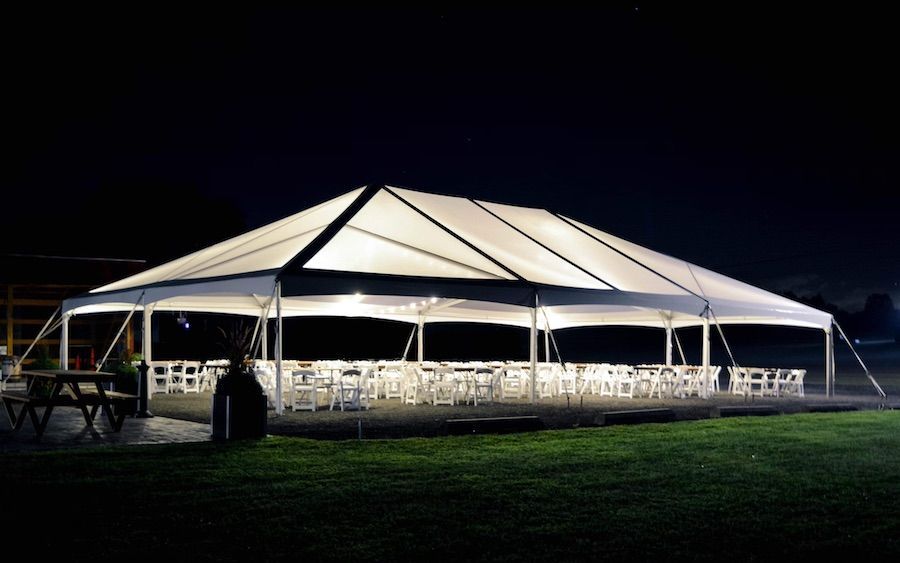 A large tent with tables and chairs underneath it is lit up at night.