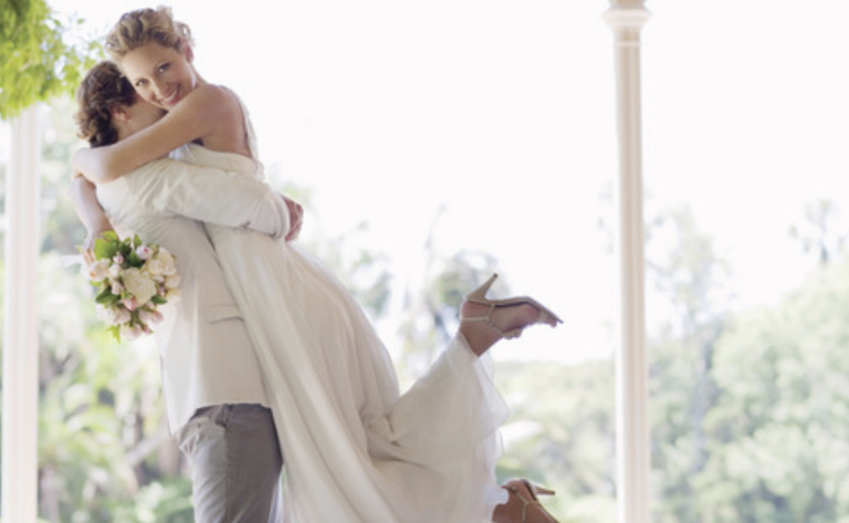 A man is holding a bride in his arms on a porch.