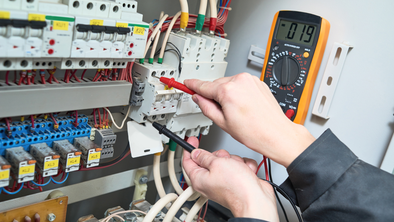 Electrician using a multimeter to test wiring in an electrical panel, digital display reads .019 volts.