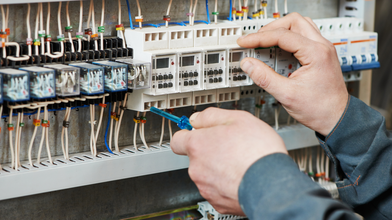 Technician adjusting electrical wiring in a control panel with circuit breakers and relays