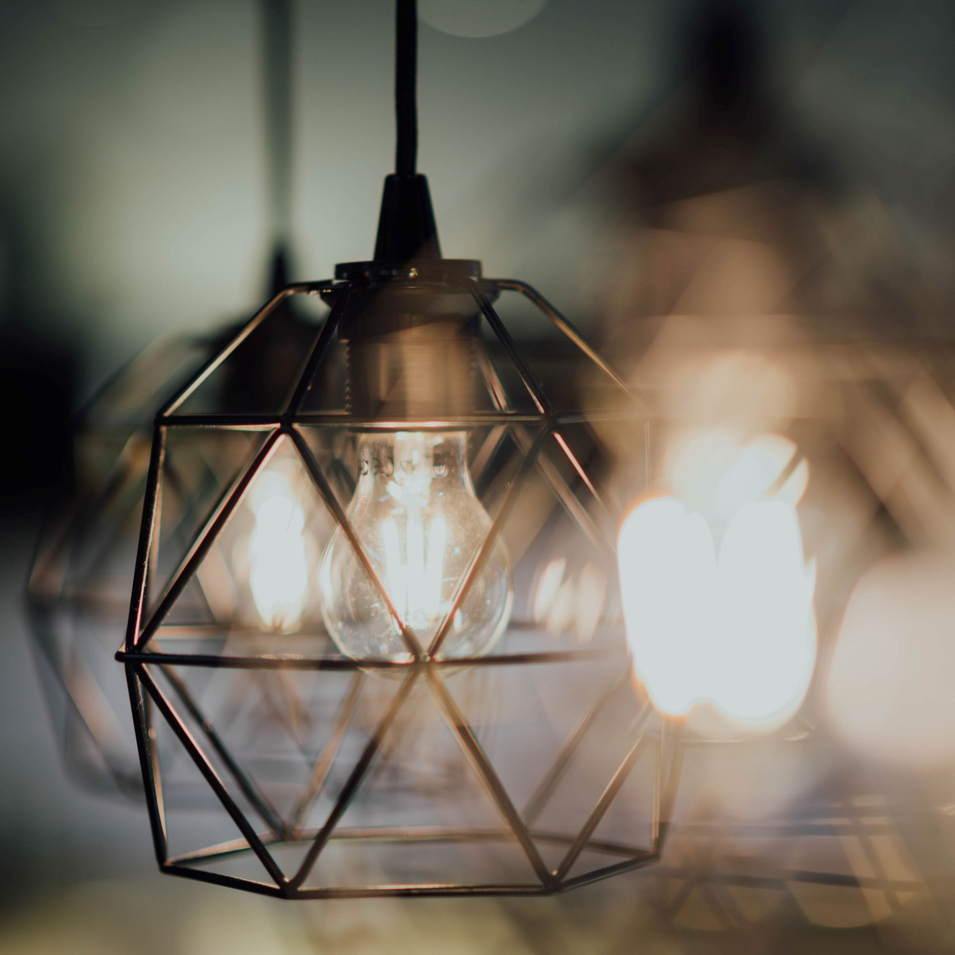 Geometric black pendant lamp with a glowing bulb, softly blurred lights in the background