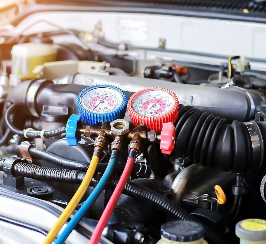 Gauges connected to car engine, showing pressure. Blue and red hoses, testing A/C system.