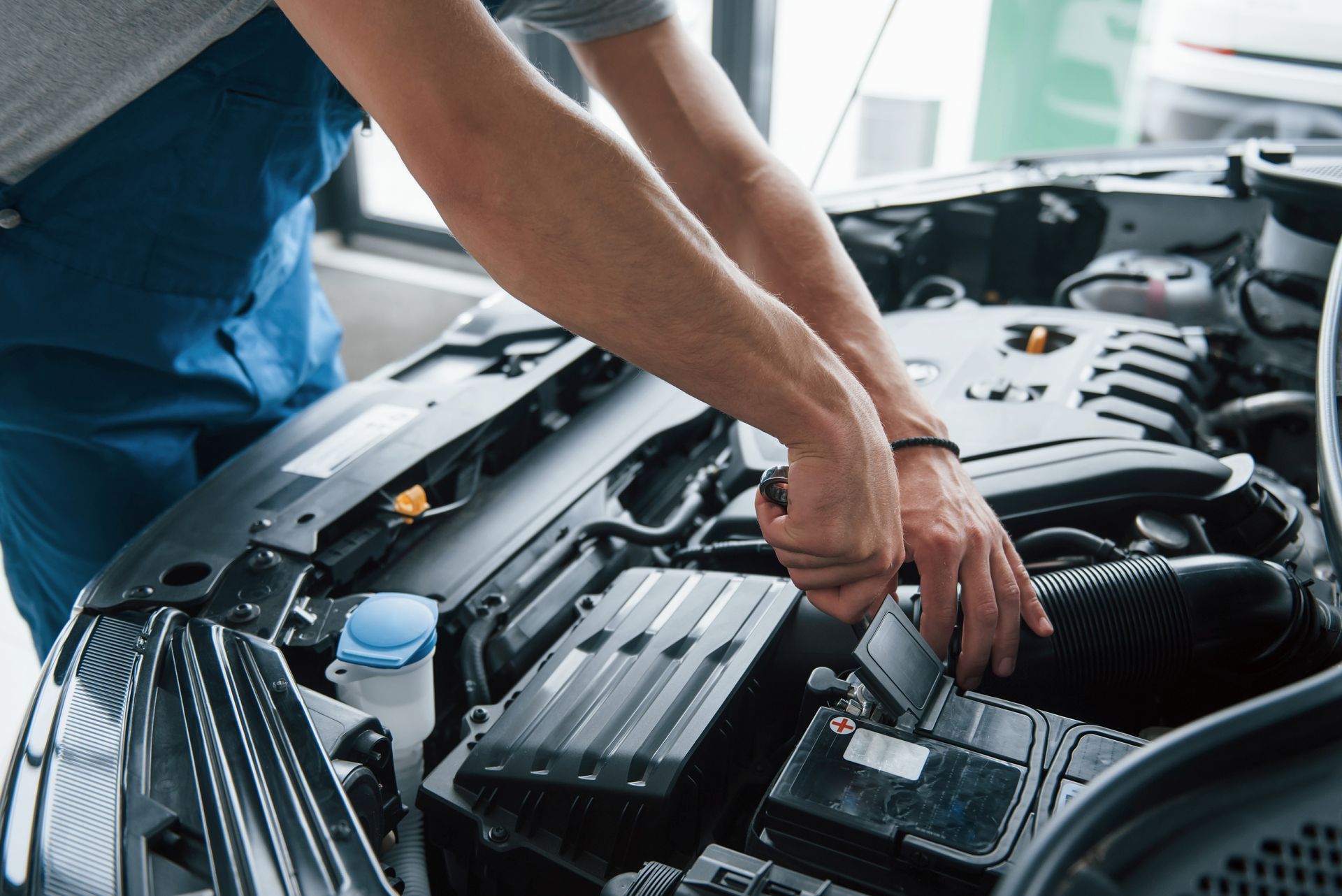 Mechanic in blue overalls works on a car engine, using a wrench. Automotive setting.