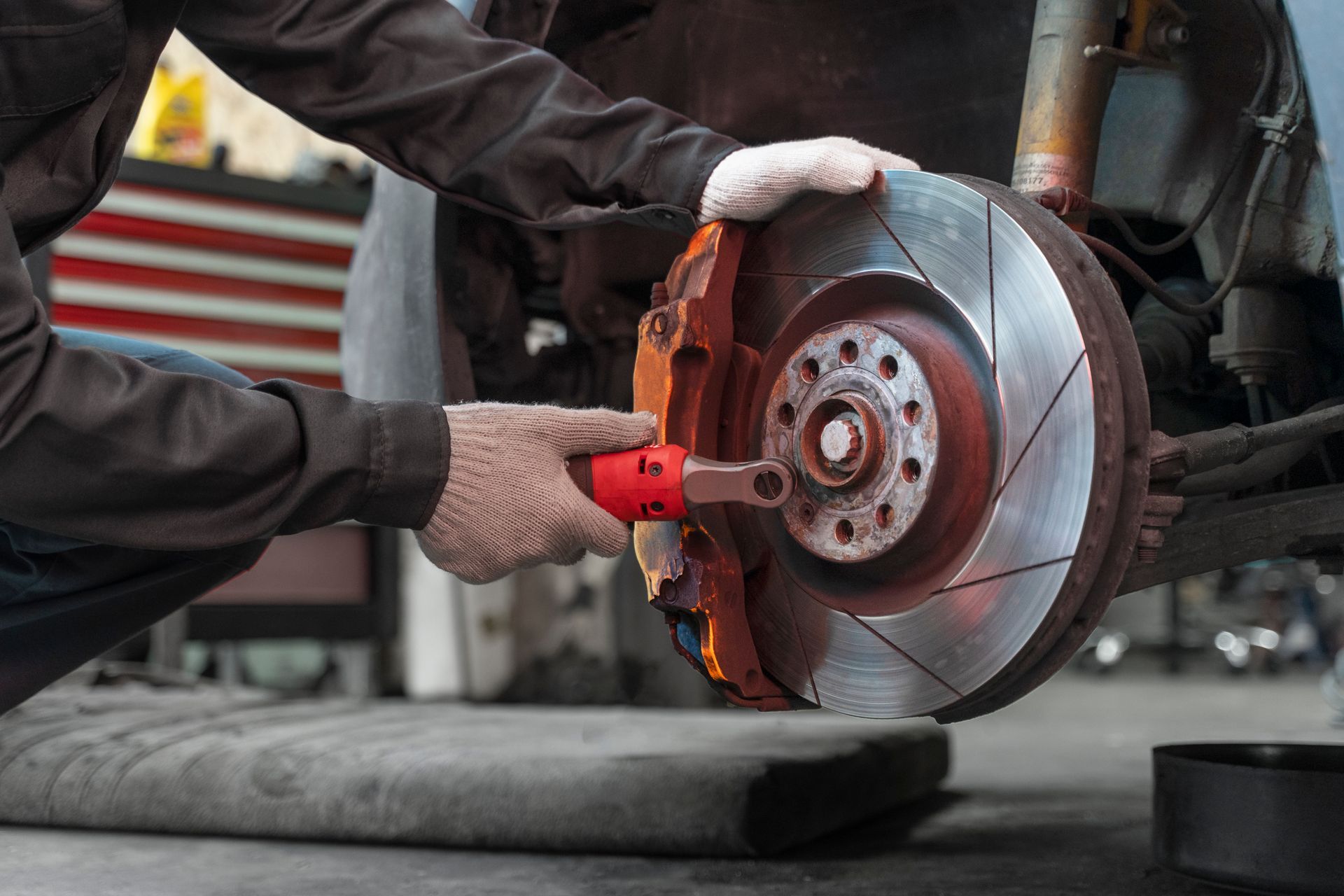 Mechanic working on a car's brake disc with red caliper, in a garage.