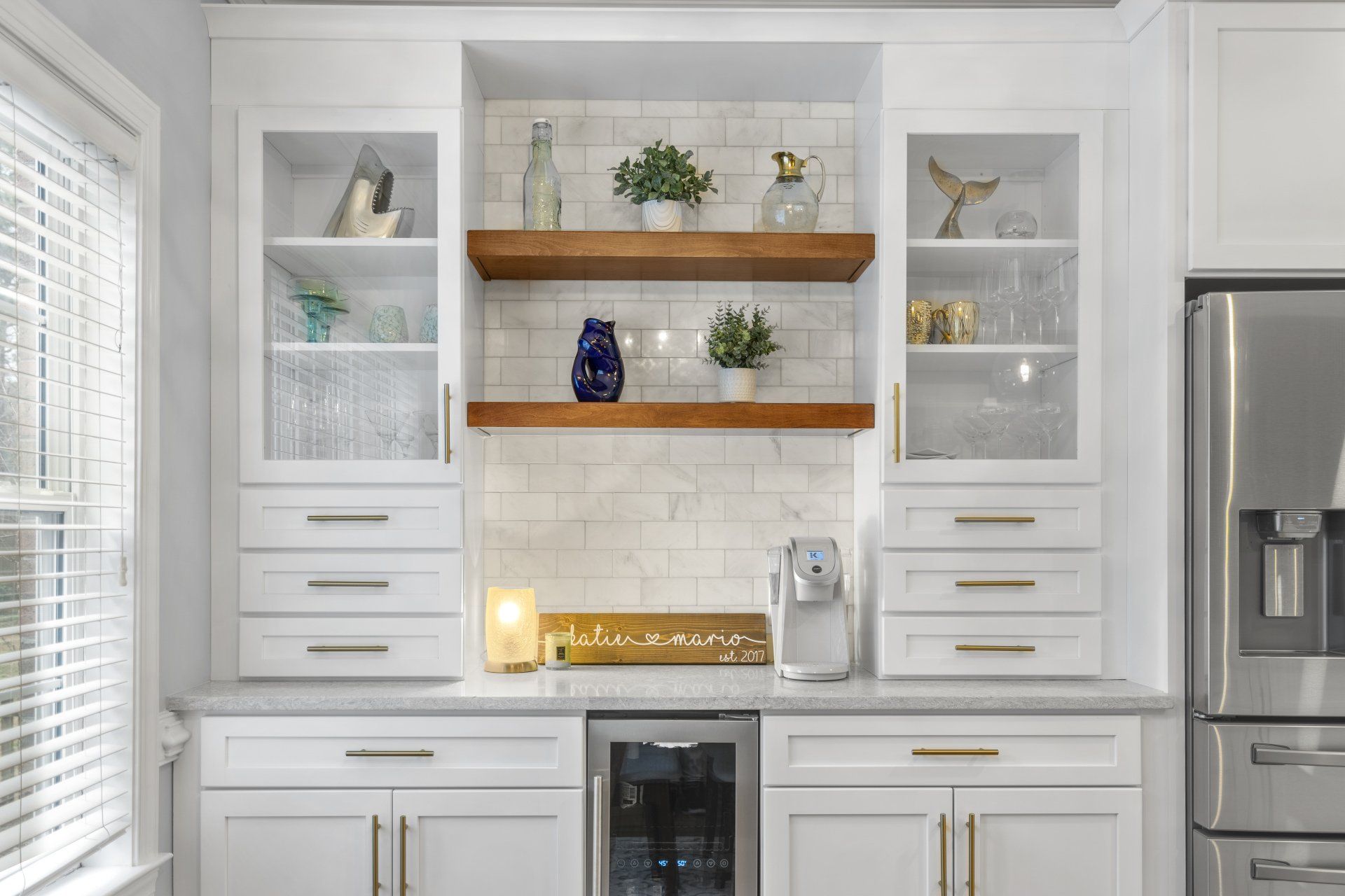 Custom kitchen with stained floating wood shelves, wine cooler, and white shaker custom cabinets for ample storage space.