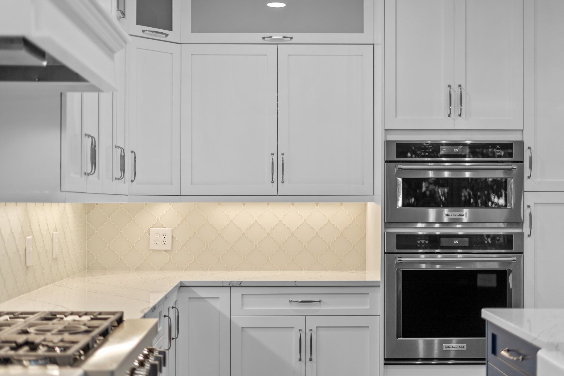White shaker cabinet kitchen with tile backsplash and double wall oven.