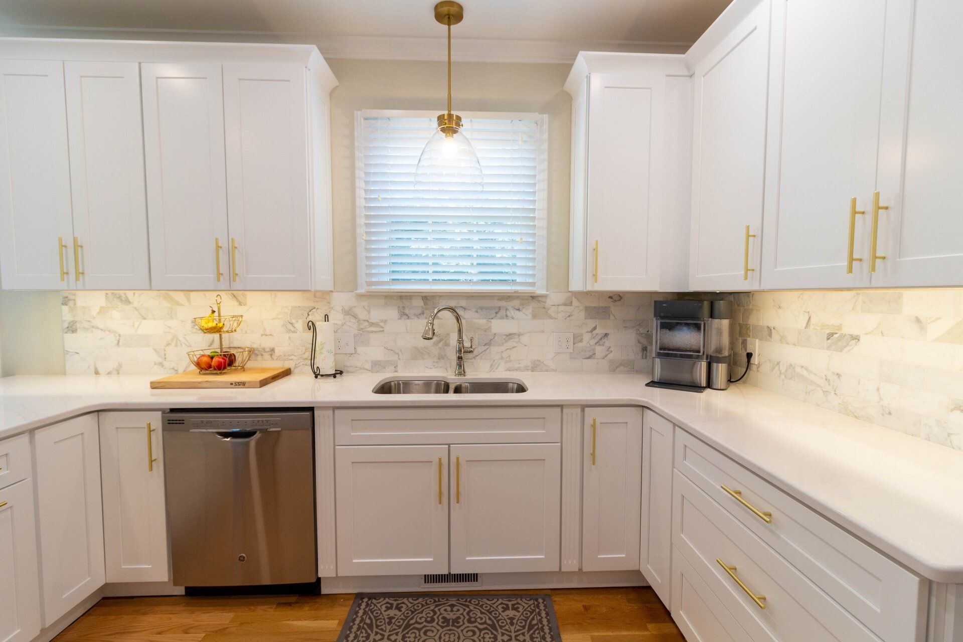 White and gold kitchen with gold pendant light over sink and marbled wile backsplash.