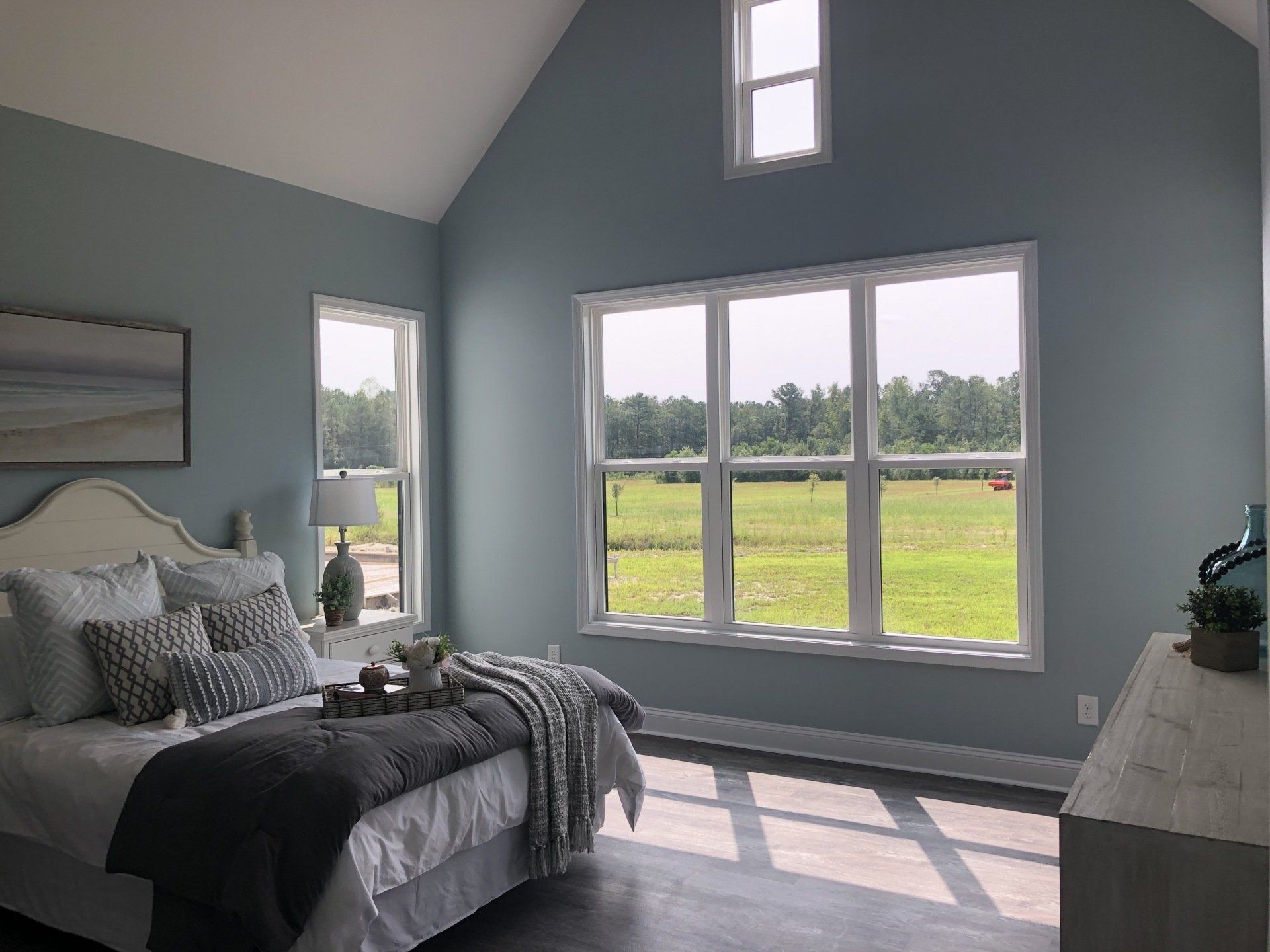 Primary bedroom featuring a large window offering natural lighting, king sized bed, and coastal blue walls.