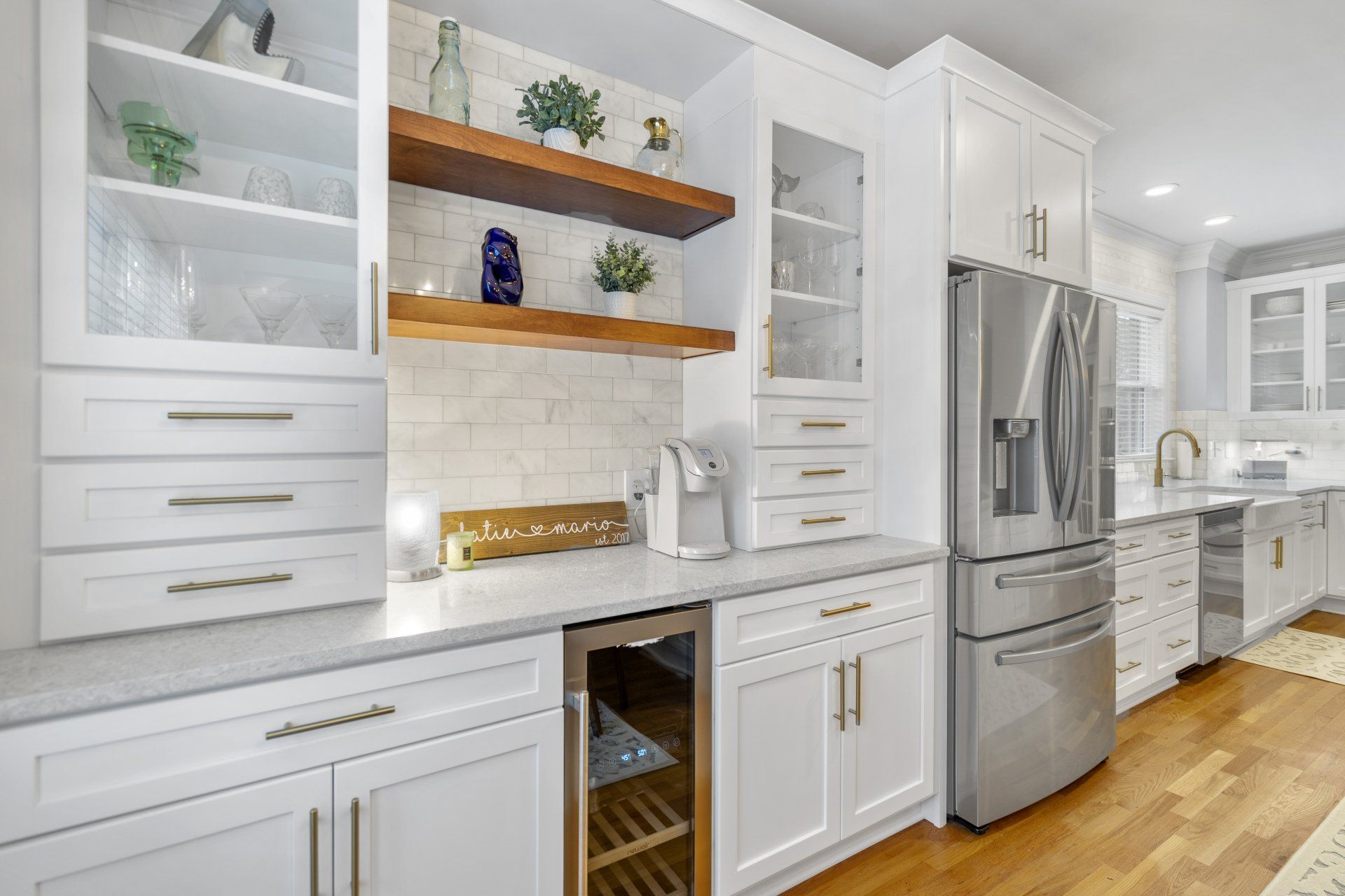 Farmhouse style kitchen remodel featuring floating shelves, white cabinets with gold hardware, and a wine cooler.