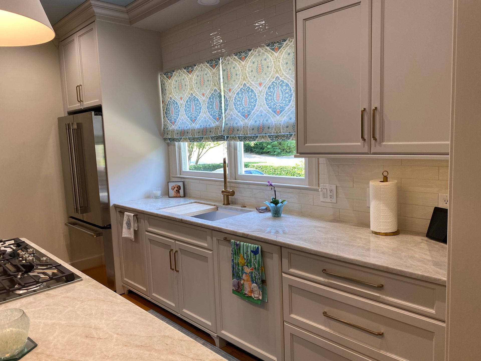 White shaker kitchen with gold hardware and plumbing fixtures and paneled dishwasher.