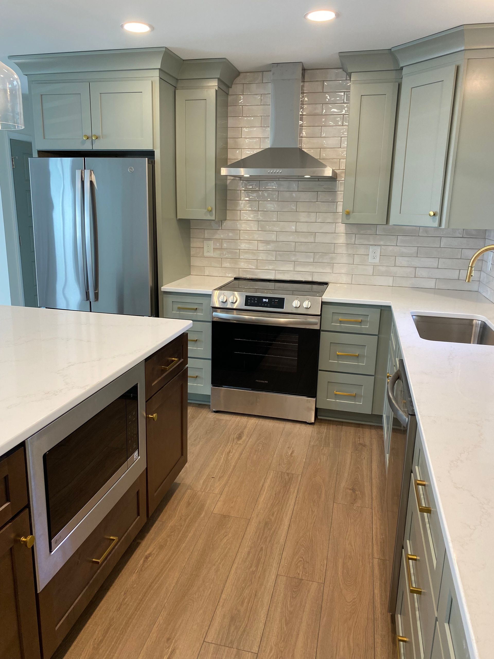 Kitchen with built-in microwave in natural wood island contrasting with moss green kitchen cabinets.