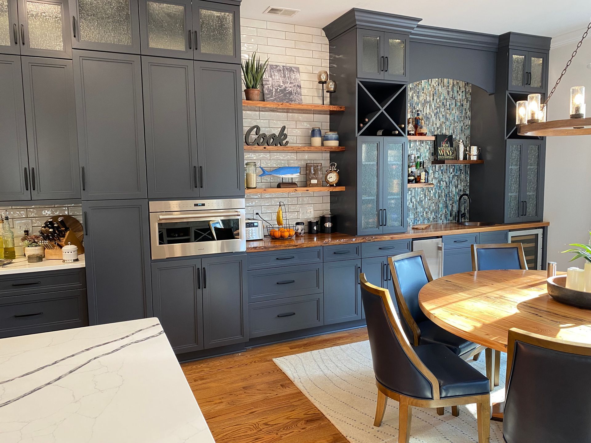 Dark blue painted cabinets with white undulated tile backsplash behind floating shelves and