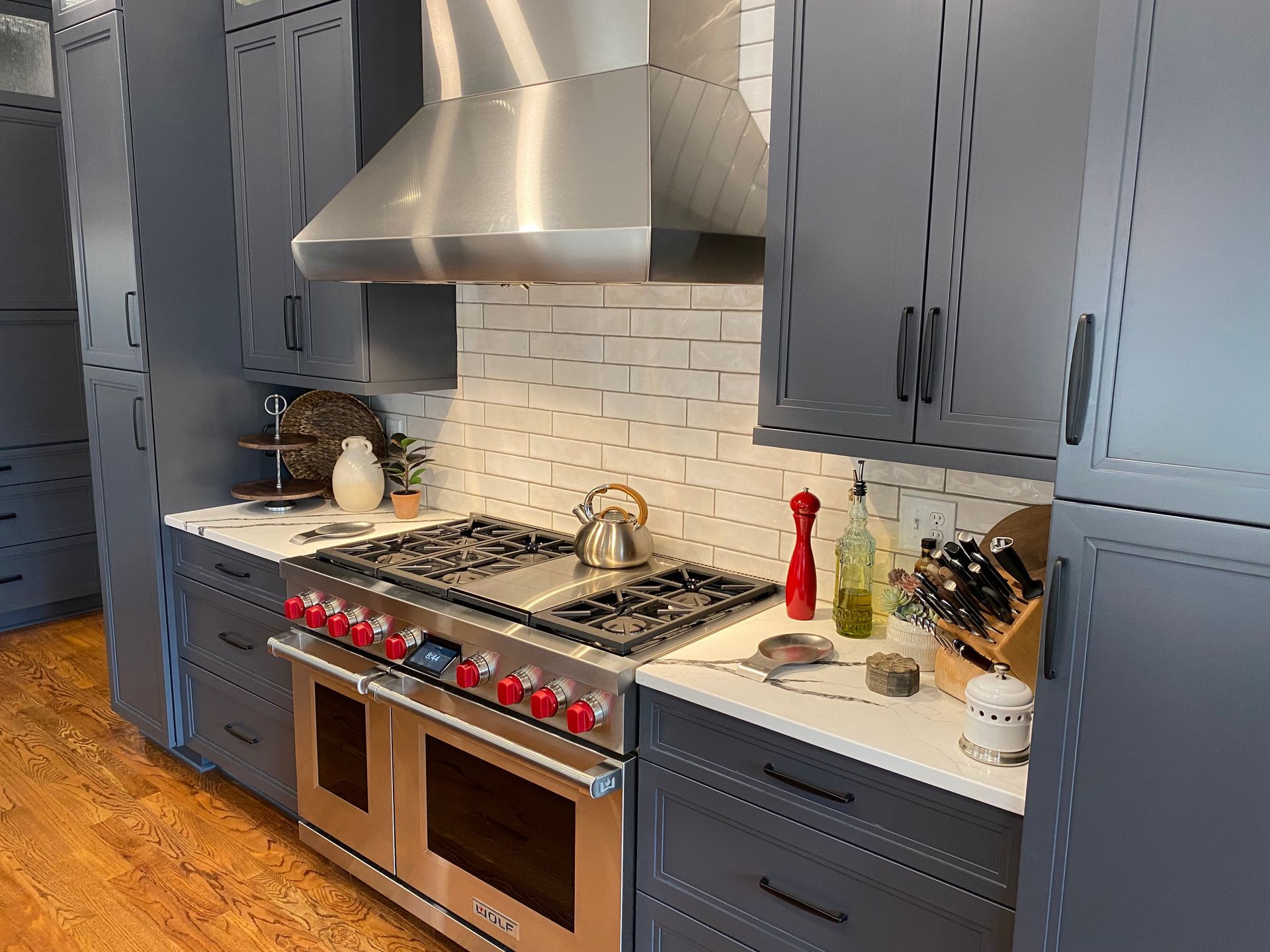 Dark blue kitchen with white subway tile backsplash, Wolf range, and matching stainless steel range hood.