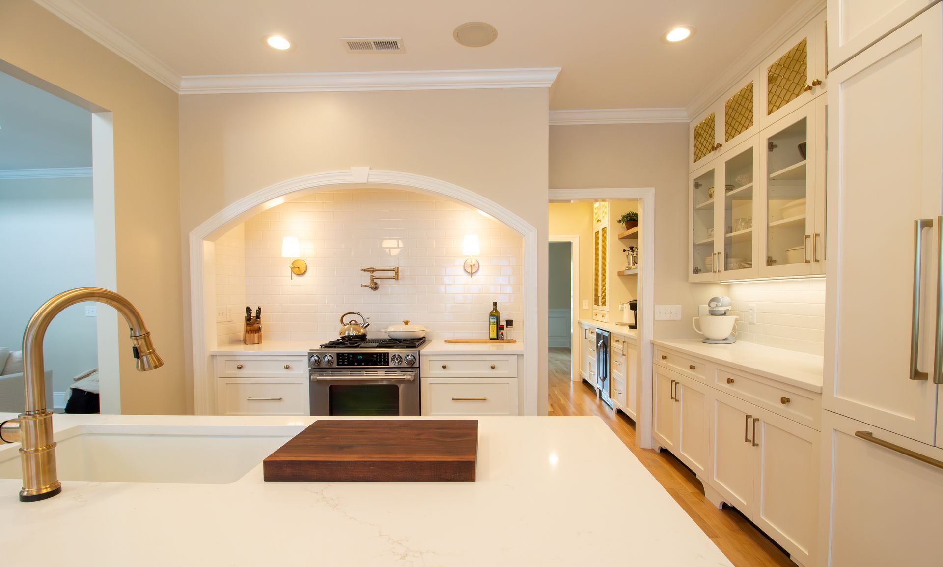 Warm white and gold kitchen with island and arched stove nook.