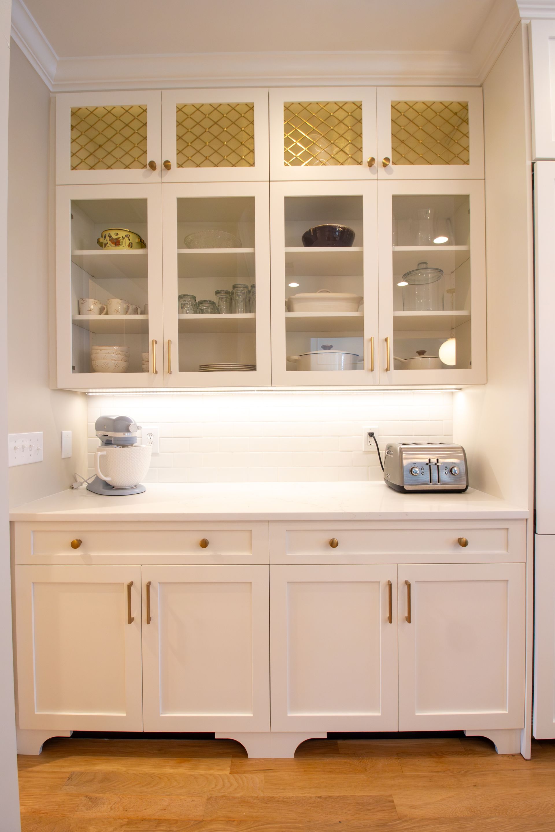 White shaker cabinets with glass door uppers, gold hardware, and gold wire mesh accents.