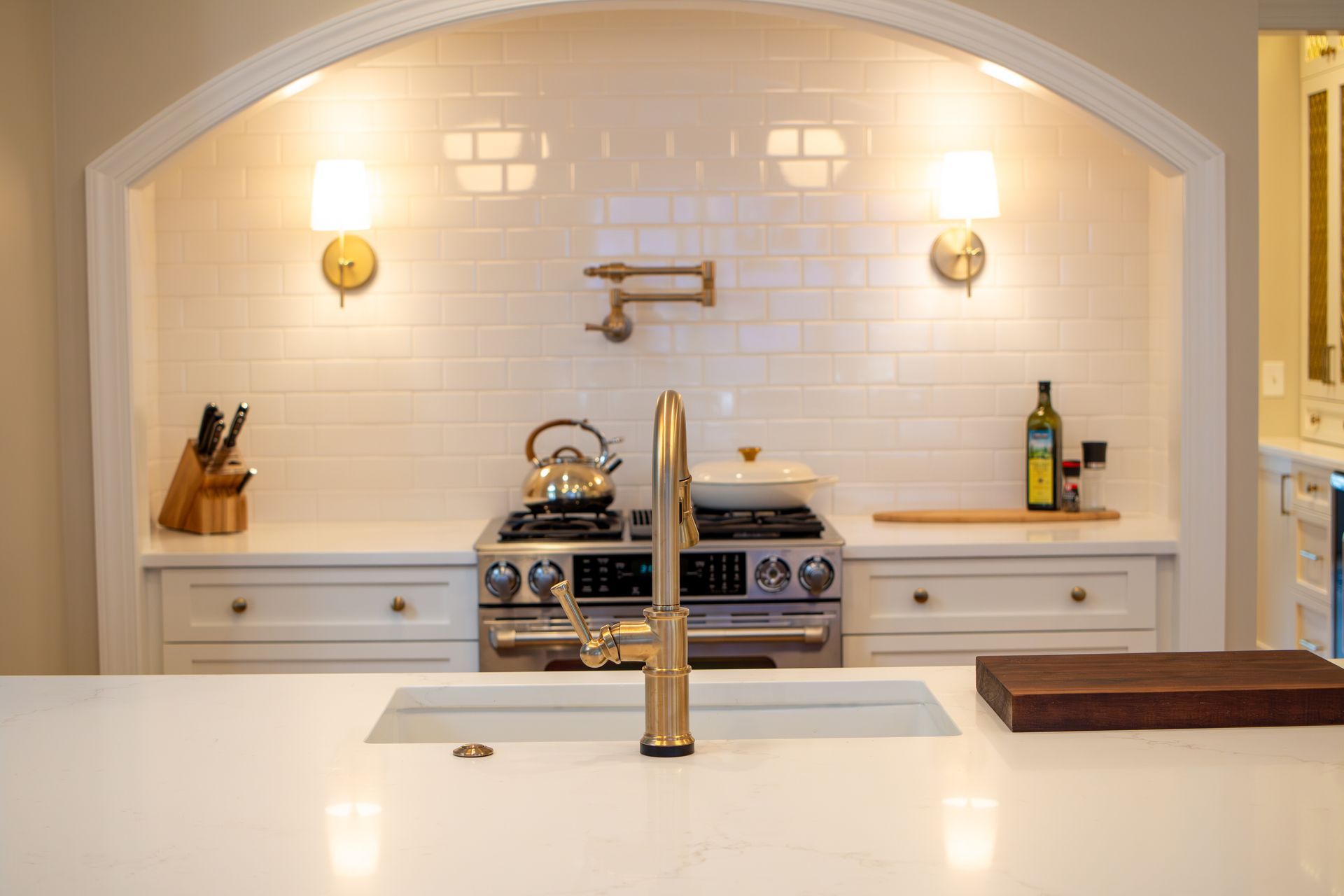 Arched cooking alcove in kitchen with gold wall sconce lights and pot filler.