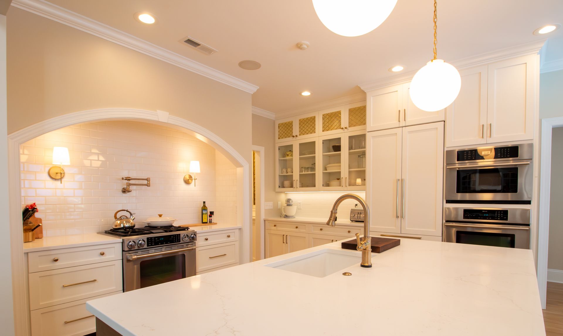 Wide view of kitchen showing cozy white cabinets with gold fixtures and accents.
