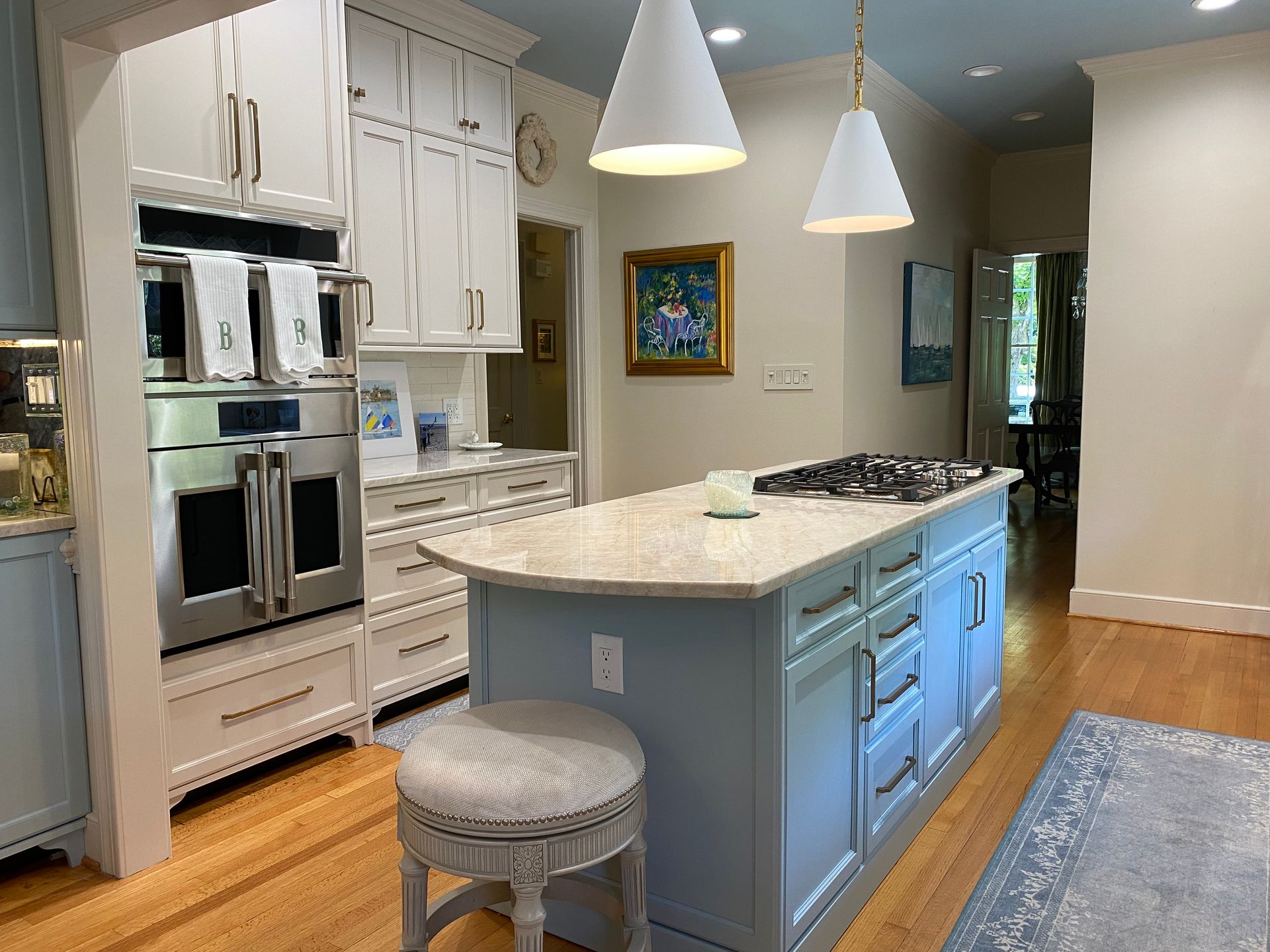Kitchen with double wall ovens, coastal blue island, and white shaker wall cabinets.